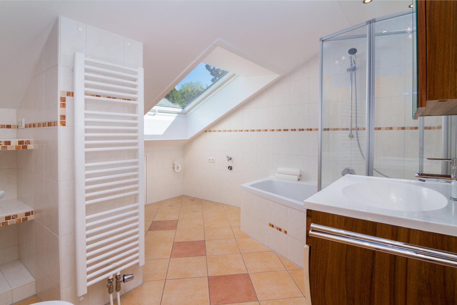 Ein modernes Badezimmer mit einem Dachfenster und schönen Fliesen an den Wänden und auf dem Boden