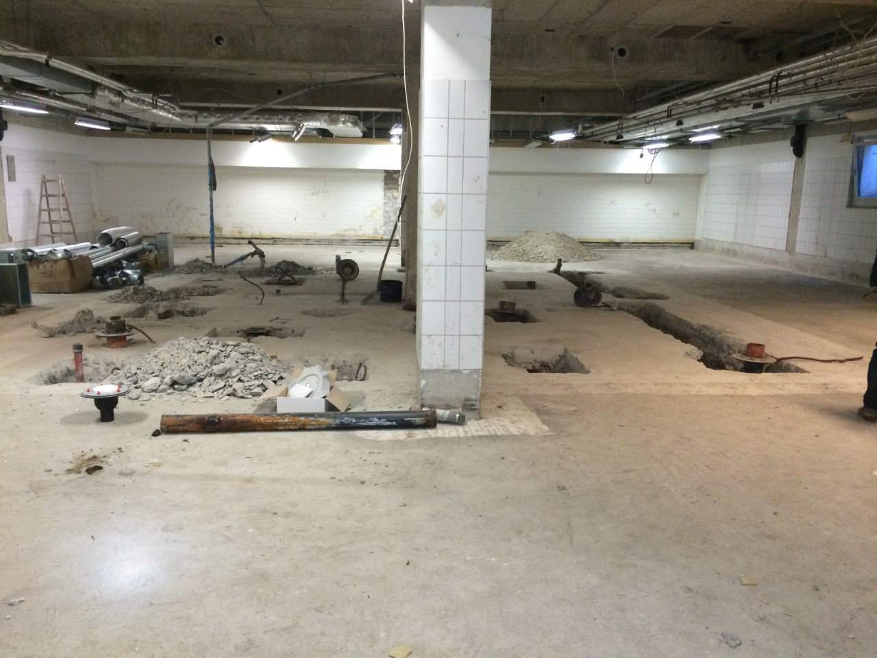 Eine große Kellerbaustelle mit Löchern im Boden, Schutt und Bauwerkzeugen, die auf der Baustelle verteilt sind