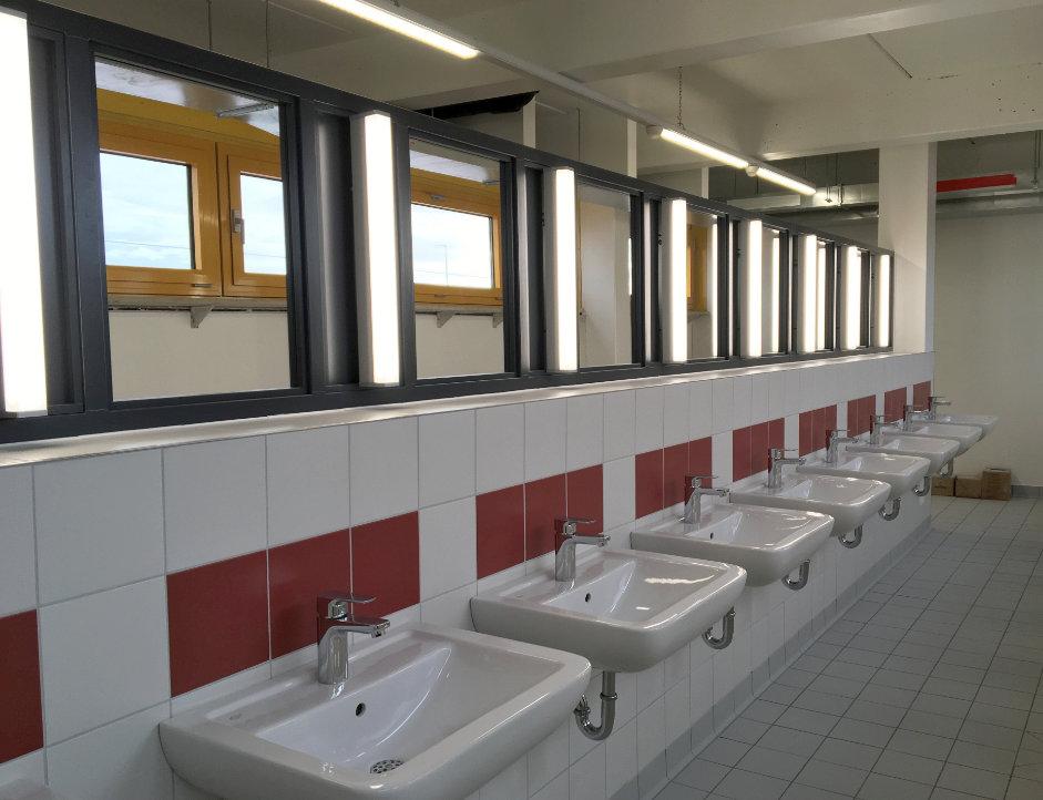 Ein Waschraum mit 8 Waschbecken an einer weiß und rot gefliesten Wand